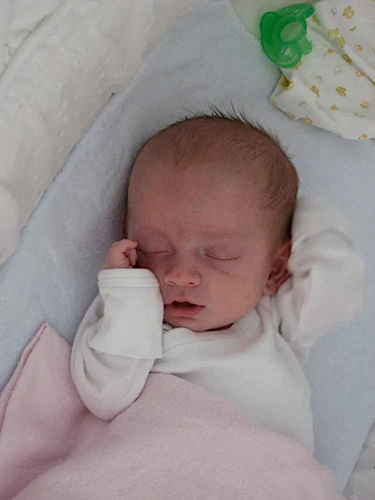 Asleep with both arms raised above his head, one fist against his cheek, a pacifier resting nearby.