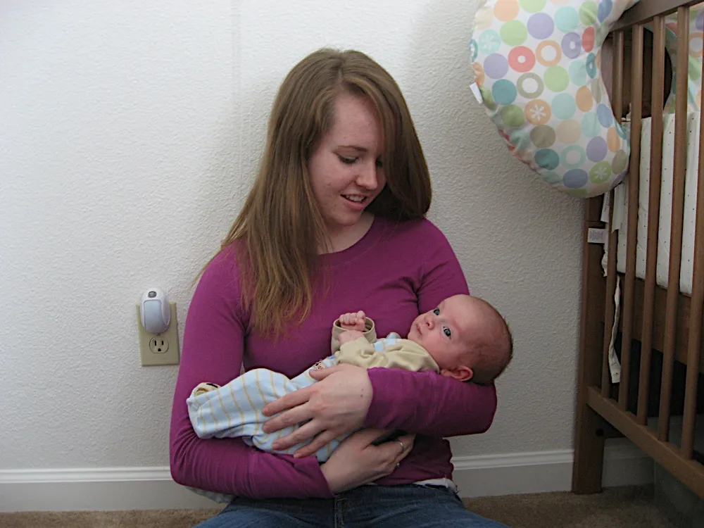Cradled in a woman's arms beside his crib, eyes open and alert.
