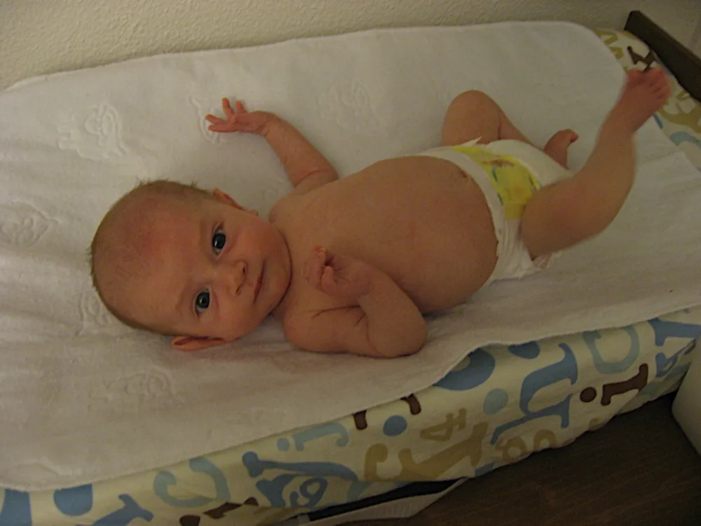 Kicking his legs up in the air on the changing pad, hands near his chin.