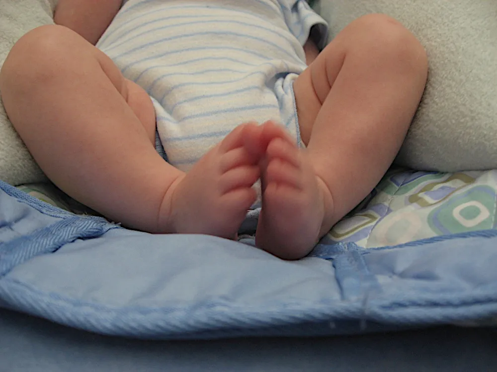 Close-up of his bare feet and legs, toes touching together, in a striped onesie.