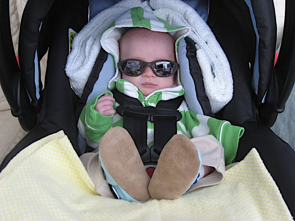 Buckled into his car seat wearing sunglasses and a green striped hoodie, ready for an outing.