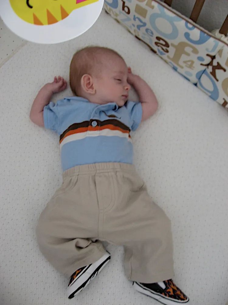 Asleep in a striped polo shirt and tiny flame-print sneakers, one hand by his ear.