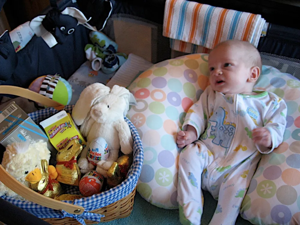 Propped on a pillow beside an Easter basket of chocolate and stuffed animals, in a dinosaur sleeper.